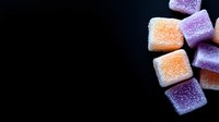 Colorful sugar jelly candies in orange and purple colors scattered on dark background with copy space, macro food photography for confectionery marketing.