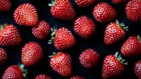 Fresh ripe strawberries scattered on dark background, macro shot showing detailed texture and natural pattern of bright red berries with green stems.