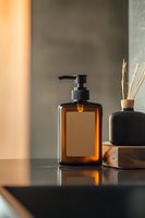 Amber glass pump bottle with blank label on reflective surface, styled with minimalist decor and natural light for spa, cosmetic, or bathroom product mockup.