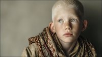 Young blonde boy with serious expression wearing knitted scarf and sweater against neutral background for lifestyle and portrait photography projects.