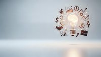 Glowing light bulb surrounded by floating business icons including dollar signs, charts, graphs and briefcase on clean white surface for innovation concepts.
