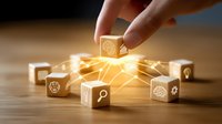 Hand placing wooden cube with glowing business icons connecting in network on wooden surface, illustrating digital transformation and business strategy.