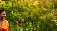 Woman with dark hair and medium skin tone wearing bright orange clothing smiling in blooming garden with colorful flowers and green foliage for lifestyle and wellness content.