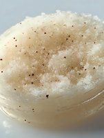 Homemade sugar body scrub with brown speckles in clear container, used for spa treatments and skincare routines.