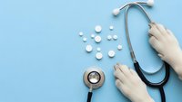 Medical stethoscope with white pills and hands on blue background for healthcare and medicine concepts.