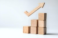 Wooden blocks arranged as ascending stairs with upward arrow symbol, representing growth, success and progress on white background. Business concept.