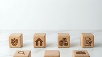 Insurance protection concept with wooden blocks showing shield, house, money and document icons on white background for financial security planning.