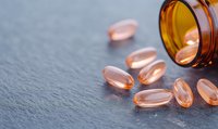 Omega-3 fish oil supplements in soft gel capsules spilled from amber medicine bottle on dark slate surface. Natural health and wellness concept for cardiovascular care.
