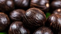 Fresh whole black nutmeg seeds in macro view showing natural texture and pattern. Dark aromatic spice background with selective focus and shallow depth of field.