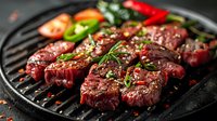 Juicy beef medallions grilling on cast iron pan with herbs, spices and fresh vegetables. Seasoned meat steaks cooking with aromatic garnish.