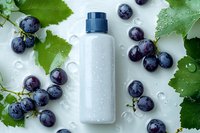 White cosmetic bottle with fresh grape berries and green leaves on wet surface, water drops scattered around, natural skincare product mockup for beauty industry.