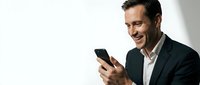 Professional businessman in suit smiling while using smartphone against white background for corporate communication and business technology concepts.
