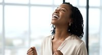 Young African American woman with long braided hair wearing a cream-colored blouse, smiling joyfully with head tilted back in a bright office setting with large windows, expressing happiness and success.
