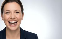 Happy businesswoman with braces smiling broadly in professional navy blazer against white background for corporate and dental care concepts.