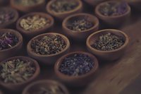 Variety of loose leaf tea types in traditional wooden bowls arranged on dark wooden surface, moody atmospheric lighting creates rustic tea ceremony ambiance.