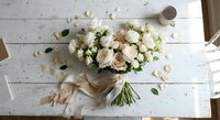 Fresh white and cream rose bouquet with eucalyptus leaves wrapped in beige ribbon on rustic wooden table, wedding floristry arrangement for bridal ceremonies.