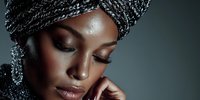 African woman wearing traditional black headwrap with elegant jewelry and natural makeup in studio portrait for beauty and cultural fashion concepts.