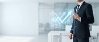 Businessman in dark suit pointing at upward trending arrow graph on transparent digital display in modern office environment, representing financial growth and business success.