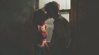 Young couple sharing intimate moment by window with warm natural light creating romantic atmosphere for relationship and love concepts.