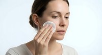 Young woman applying facial cleanser with cotton pad for daily skincare routine and beauty treatment at home.