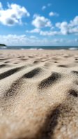 Close-up of sandy beach with textured ripples against blurred ocean and blue sky with fluffy white clouds, ideal for summer vacation themes.