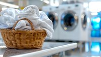 Fresh white laundry piled in wicker basket at modern laundromat with washing machines in background, focus on foreground basket for commercial use.