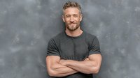 Confident middle-aged Caucasian man with beard smiling with crossed arms against concrete wall background for lifestyle and business concepts.