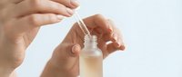 Close-up of hands holding dropper bottle with serum or essential oil against white background for skincare, cosmetics, and beauty product marketing.