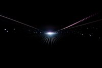 Glowing light rays pierce through darkness creating dramatic perspective effect with bright center point and radiating beams against black background.