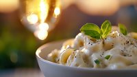 Creamy macaroni pasta in white ceramic bowl garnished with fresh basil and black pepper against blurred golden bokeh background, comfort food styling.