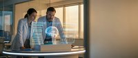 Two medical professionals examining holographic brain scan data on laptop in modern hospital office for neurological research and diagnosis consultation.