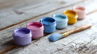 Colorful acrylic paint jars in pastel shades arranged in row with paintbrush on rustic wooden surface. Artistic composition for creative projects and crafts.