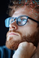 Young bearded man in glasses looking up thoughtfully with glowing network visualization effects above, representing innovation and digital transformation.