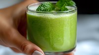 Fresh green smoothie with mint garnish in glass, selective focus on frothy beverage surface showing healthy lifestyle and detox drink concept.