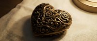 Ornate bronze heart-shaped locket with intricate floral filigree detailing rests on neutral fabric, perfect for vintage jewelry, antique collections, and decorative design projects.