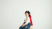 Young Asian woman wearing traditional Korean hanbok with red jacket and blue skirt, sitting against white background. Suitable for cultural fashion, heritage celebrations, and traditional clothing design projects.