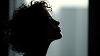 Silhouette profile of young woman with curly hair against window light, creating dramatic contrast between dark figure and bright background.