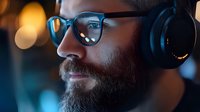 Professional bearded man with glasses and headphones working in modern office environment with warm bokeh lighting effects.