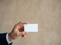 Male hand in business suit holding blank white card against neutral beige background, suitable for corporate branding, business card mockups, and professional presentations.
