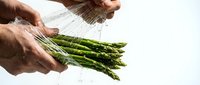 Male hands rinsing fresh green asparagus under running water against white background. Healthy vegetable preparation for cooking and food preparation.