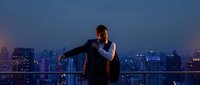 Young businessman in suit standing on rooftop terrace overlooking illuminated city skyline at dusk, urban professional lifestyle and success concept.
