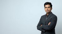 Young South Asian male professional wearing dark gray button-up shirt, arms crossed, confident posture, studio portrait against white background for corporate and business use.