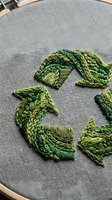 Green botanical leaf embroidery on gray linen fabric in wooden hoop showcasing detailed needlework stitches for handmade textile art and craft projects.