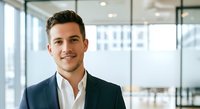 Young male professional with dark hair and light skin tone wearing navy blazer and white shirt, smiling confidently in modern office with glass partitions and city views, suitable for corporate business and leadership concepts.