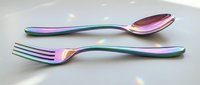 Iridescent rainbow cutlery set with holographic finish on white background, modern kitchen utensils with colorful metallic coating for dining and food service.