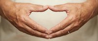 Elderly hands forming heart shape gesture showing love care and compassion in warm lighting for healthcare wellness and family concepts.
