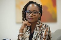 Professional African American businesswoman with glasses smiling confidently in modern office environment, hand on chin in thoughtful pose for corporate success.