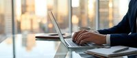 Businesswoman with brown skin typing on laptop at modern office desk with city skyline view, professional work environment for corporate business and technology concepts.