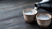Japanese sake being poured from ceramic bottle into traditional cups on rustic wooden table, creating authentic dining atmosphere.