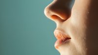 Close-up profile view of feminine lips and nose against turquoise background, showing natural skin texture and soft coral lipstick in dramatic side lighting.